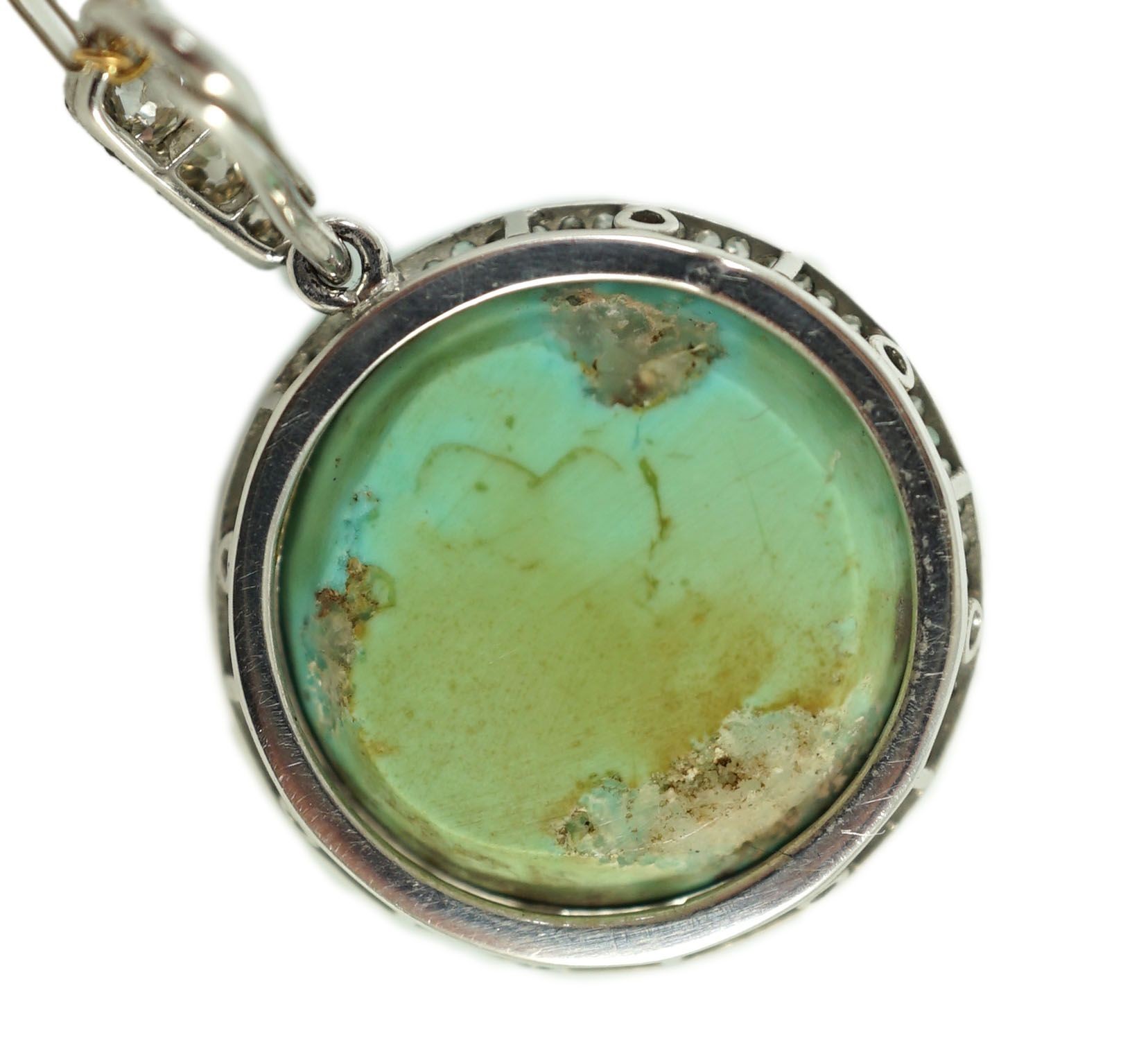 An early 20th century platinum and turquoise set pendant, with diamond chip border and diamond set bale, on a 15ct two colour gold fine link chain
